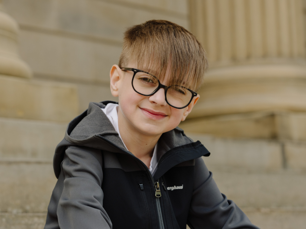 A young boy wearing a black jacket and white shirt, sitting on a stair case.