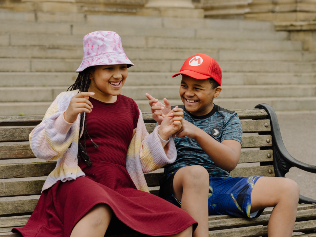 Two children laugh together on a park benich.