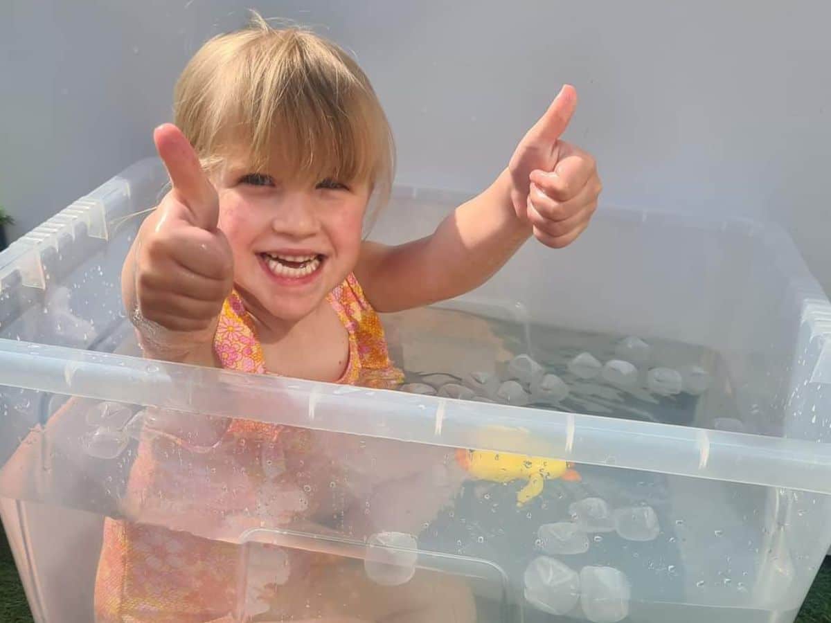 A little girl is sitting in a tub of water with some pretend ice cubes in it.