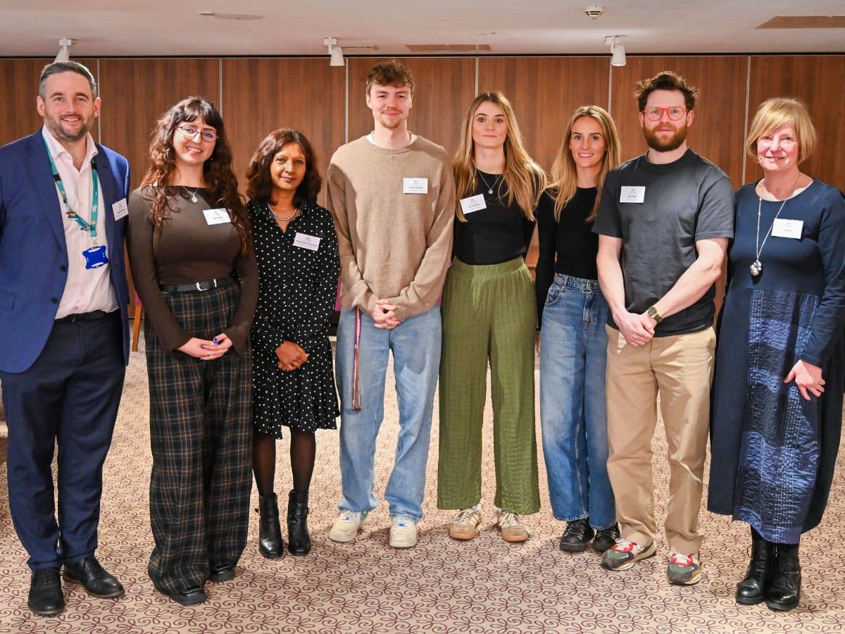 A group of people stand in a wooden panelled room. They are side-by-side and smiling for the camera.
