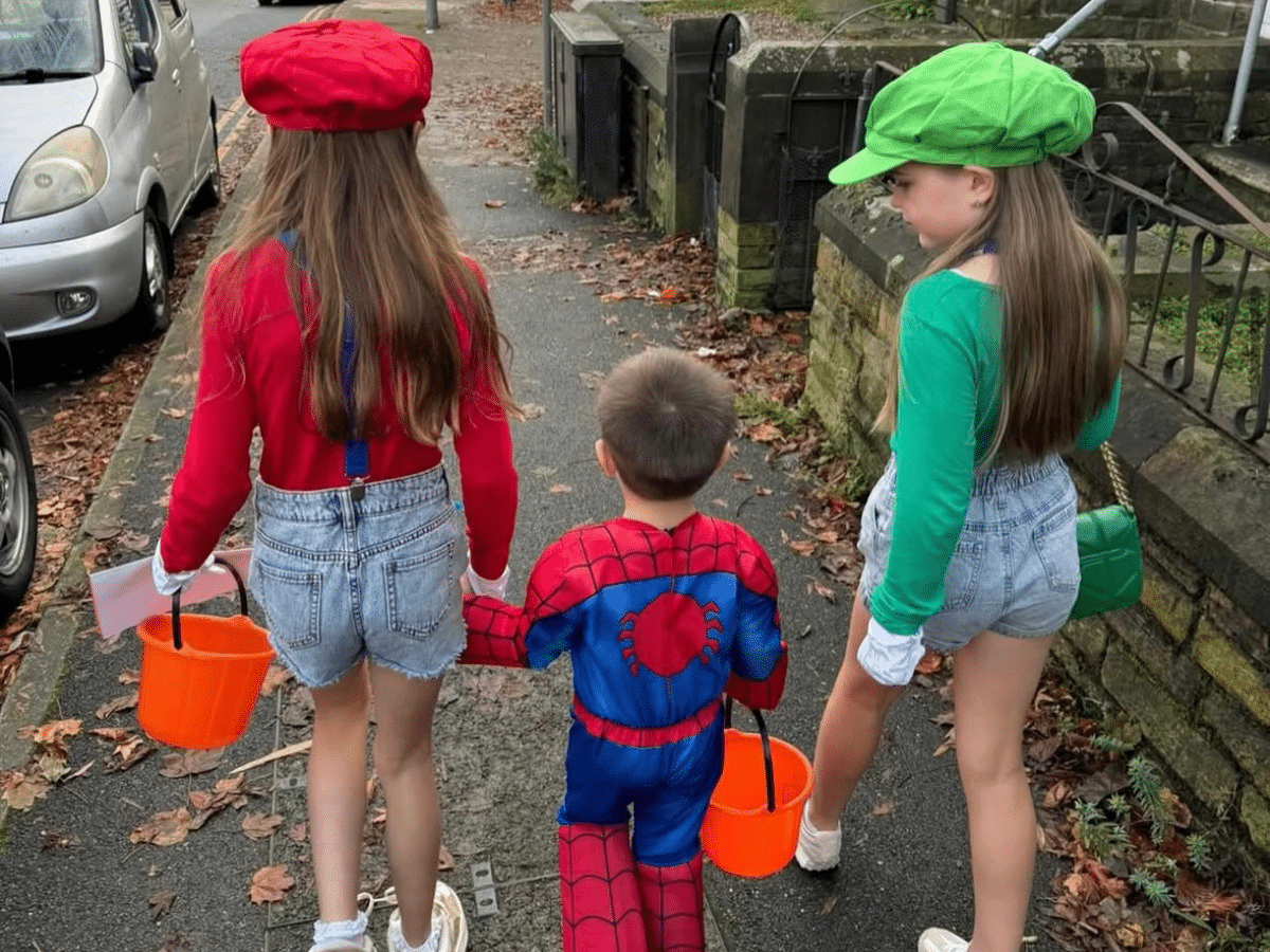 Three children are out trick or treating. The two girls are dressed as Super Mario and Luigi, and the little boy is dressed as Spider Man.