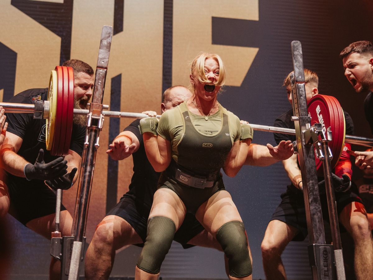 A lady is lifting some really heavy weights and there is a group around her cheering her on.